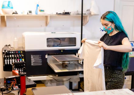 Young oung woman prepares to decorate blank t-shirts using a direct-to-garment printing machine